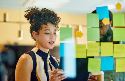 A man and a woman are standing in front of a glass wall writing on sticky notes.